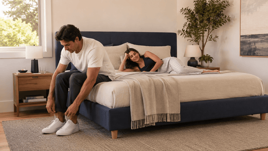 A realistic modern Australian bedroom showing one person sitting naturally on the mattress edge while another lies near the opposite side.